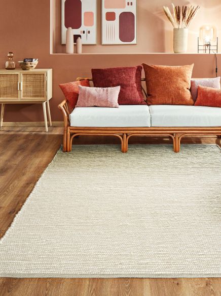 Sofa mit Kissen steht vor pastellrosa Wand mit Kunstwerken und Dekorationen in modernem Wohnzimmerambiente