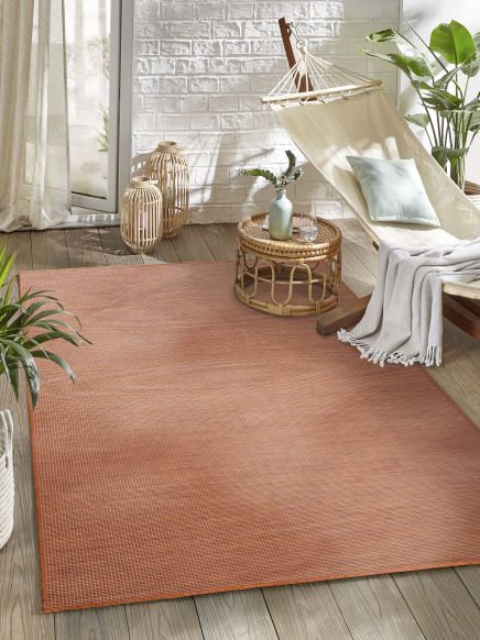 Roter Teppich liegt auf Holzboden, daneben Pflanzen, Hängematte und Korbtisch mit Vase.