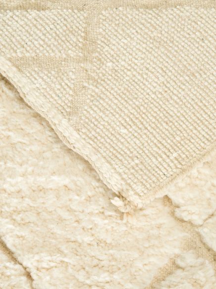 Tuch liegt aufgefaltet auf einem flauschigen Teppich, beide in cremefarbenen Tönen.