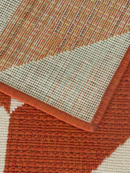 Teppich zeigt die Unterseite mit farbigem Gewebe und obere Seite mit rotem Muster und Fransen.