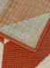 Teppich zeigt die Unterseite mit farbigem Gewebe und obere Seite mit rotem Muster und Fransen.