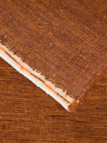 Brauner Teppich zeigt Rückseite mit Kante und Textur, auf gleicher brauner Oberfläche liegend.