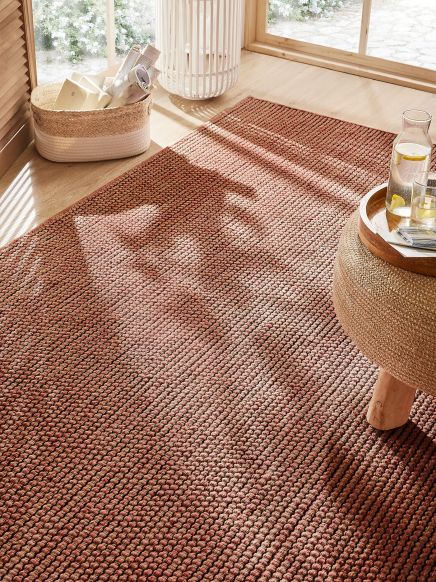 Roter Teppich liegt auf Holzfußboden, daneben Korb mit Zeitungen und Tisch mit Wasser und Glas.
