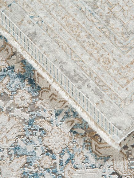 Teppich zeigt gemustertes florales Design in Blau, Beige und Grau, Ecke umgeklappt.