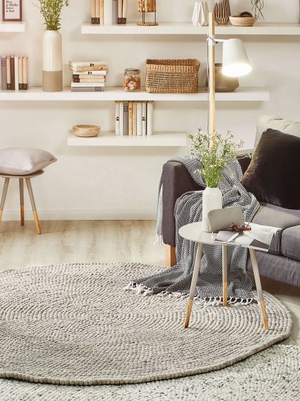 Runder Teppich liegt unter einem kleinen Tisch mit Vase und Zeitung im gemütlichen Wohnzimmer.