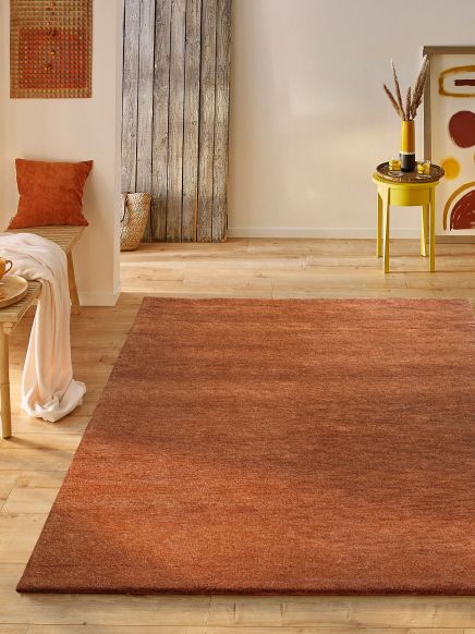 Roter Teppich liegt auf Holzfußboden, daneben gelber Beistelltisch mit Vase und Deko im Raum.