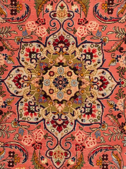 Orientalischer Teppich zeigt symmetrisches Blumenmuster mit roten, blauen, cremefarbenen und grünen Details auf rosa Hintergrund.