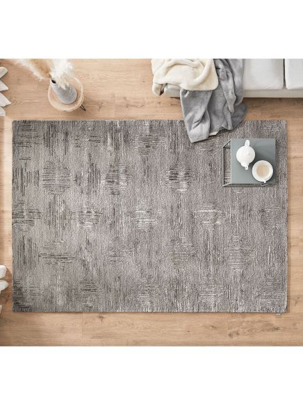 Grauer Teppich liegt auf Holzboden, daneben eine Couch mit Decke und ein Tablett mit Teekanne und Tasse.
