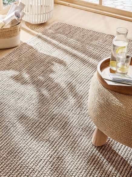 Gepunkteter Teppich liegt im Sonnenlicht, daneben ein Tisch mit Karaffe und Glas Wasser mit Zitrone.