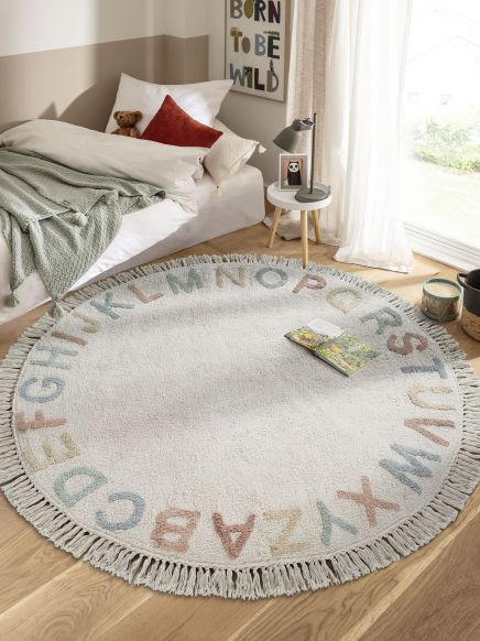 Runder Teppich mit Alphabet liegt auf Holzboden im Kinderzimmer neben Bett und Nachttisch.