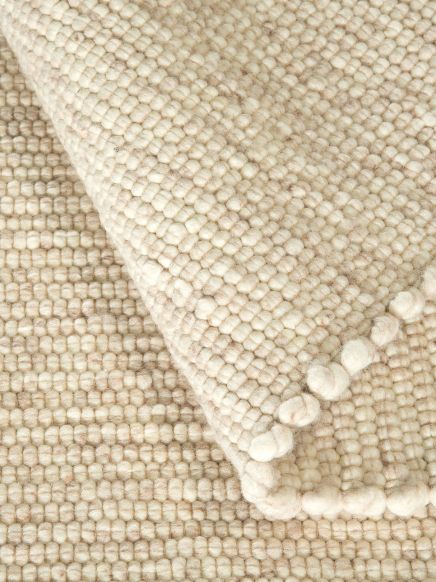 Wollteppich liegt gefaltet, zeigt strukturierte Oberfläche mit kleinen, runden Fasern in Beige und Cremefarben.