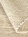 Wollteppich liegt gefaltet, zeigt strukturierte Oberfläche mit kleinen, runden Fasern in Beige und Cremefarben.