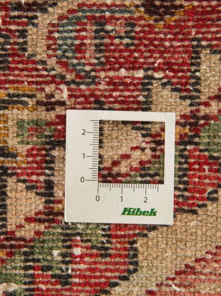 Maßstabsrahmen liegt auf bunter Teppichstruktur mit rot, grün, beige und schwarzen Mustern.