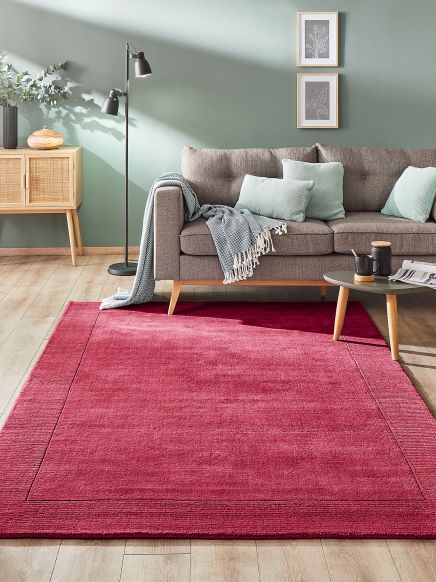 Roter Teppich liegt vor grauem Sofa mit Kissen und Decke im modernen Wohnzimmer.