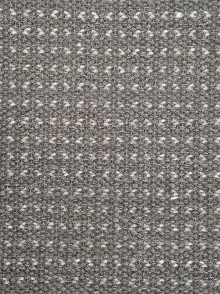 Grauer Teppich mit hellem, geometrischem Muster aus kleinen Dreiecken und Linien.