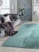 Hellblauer Teppich liegt vor grauer Couch mit Decke und Kissen in modernem Wohnzimmer.