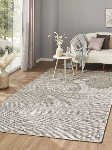 Teppich liegt auf Holzboden vor Sofa mit Kissen und Decke, kleine runde Tisch mit Vasen im Wohnzimmer.