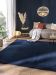 Blauer Teppich liegt auf Holzboden vor grauem Sofa mit Decke und Kissen in hellem Wohnzimmer.