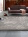 Braunes Sofa steht mit Decke und Tasche auf grauem Teppich in modernem Raum mit Stadtblick.