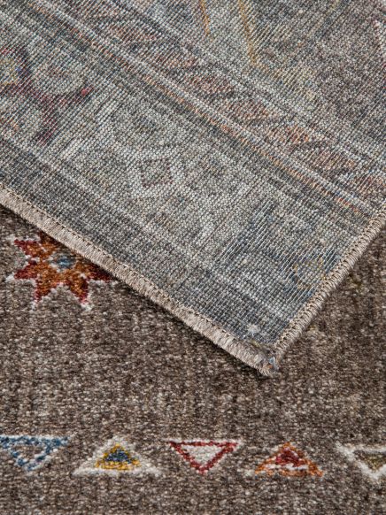 Teppich zeigt bunte geometrische Muster auf braunem Grund, Ecke nach oben geklappt.