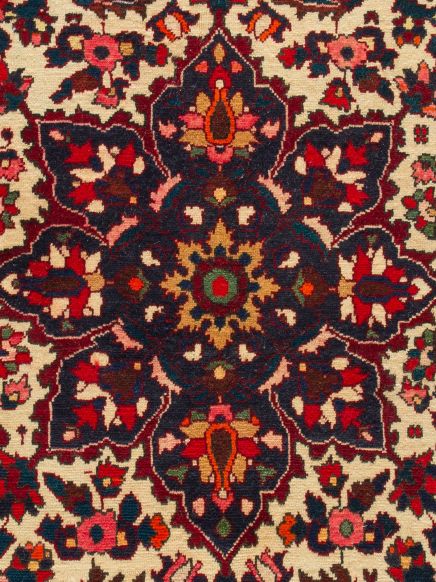 Teppich zeigt ein symmetrisches, mehrfarbiges Blumenmuster auf hellbeigem Grund.