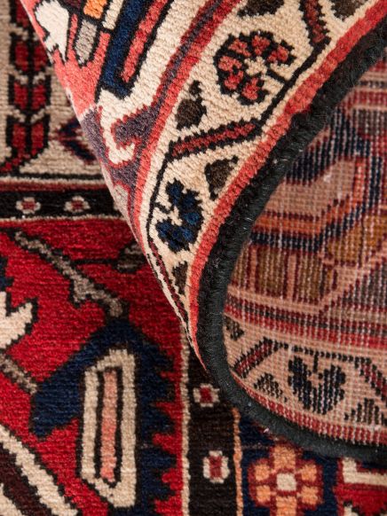 Ein gemusterter Teppich wird an einer Ecke hochgehoben, zeigt Rückseite und Vorderseite.
