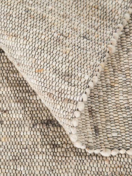 gewebter Teppich liegt gefaltet, beige und schwarze Fäden, Detailaufnahme des Musters