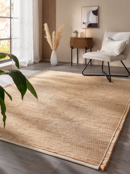 Beiger Teppich liegt auf Boden, daneben Sessel, Pflanze, Kommode mit Lampe und Vase mit Pampasgras.