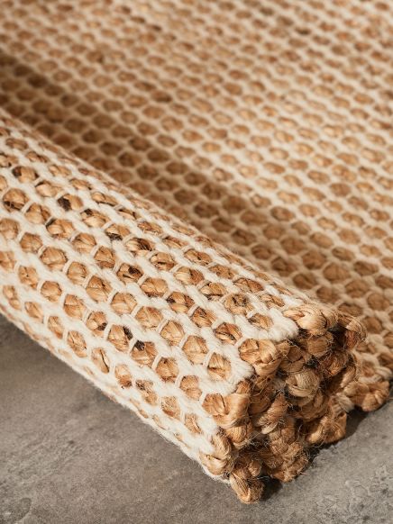 Geflochtener Teppich liegt gerollt auf grauem Boden mit grober, natürlicher Struktur.