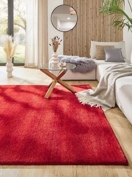 Roter Teppich liegt in Wohnzimmer vor Glas-Couchtisch und weißem Sofa mit Decke und Kissen.