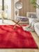 Roter Teppich liegt in Wohnzimmer vor Glas-Couchtisch und weißem Sofa mit Decke und Kissen.