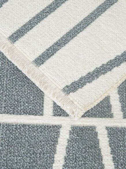 Teppich mit geometrischem Muster legt sich über einen anderen mit streifenförmigem Design.