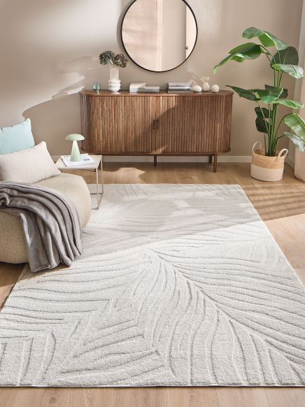 Weißer Teppich liegt auf Holzboden vor braunem Sideboard mit rundem Spiegel im modernen Wohnzimmer.