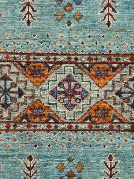 Teppich zeigt geometrische Muster und farbige Ornamente in Blau, Orange und Rot auf Textilfläche.