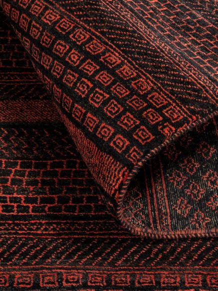 Teppich zeigt rote geometrische Muster auf schwarzem Hintergrund, Teil aufgerollt.