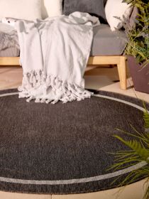 Runder Teppich mit weißem Rand liegt vor einem Sofa mit weißen Decke und Kissen in Innenraum.