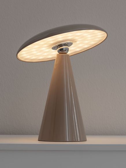 Tischlampe mit kegelförmigem Fuß leuchtet warm, steht auf glatter weißer Oberfläche vor Wand.