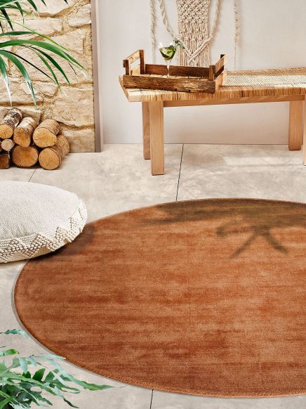 Runder Teppich liegt auf Boden, Holztisch mit Tablett und Getränk, Polster, Holzstapel, Pflanzen.