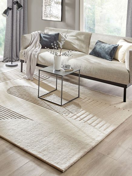 Beiges Sofa mit Kissen und Decke neben kleinem Tisch mit Vase, stehender Lampe im hellen Wohnzimmer.