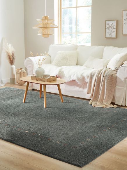 Sofa liegt mit Decke und Kissen in hellem Raum, Holztisch steht auf dunklem Teppich.