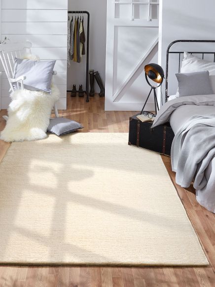 Teppich liegt auf Holzboden in Schlafzimmer mit Bett, Sessel, Kissen, Lampe und Kleiderständer.