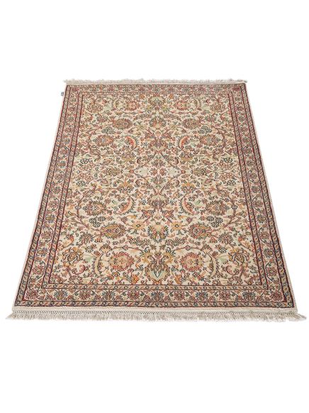 Teppich zeigt florales Muster mit Bordüre, liegt flach auf hellem Hintergrund.