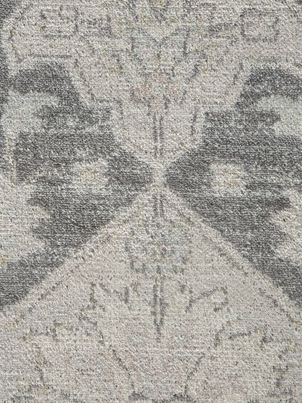 Teppich zeigt symmetrisches floral-geometrisches Muster in Grau- und Beigetönen.