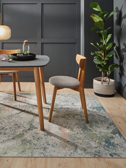 Moderner Holzstuhl steht vor Esstisch mit Glas und Kerzen, Zimmerpflanze steht an Wand.