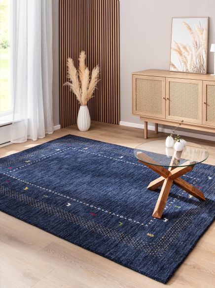 Blauer Teppich liegt auf Holzfußboden, Glas-Couchtisch steht darauf, helle Möbel und Deko im Raum.