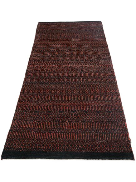 Teppich zeigt rot-schwarzes geometrisches Muster, liegt flach auf hellem Hintergrund.