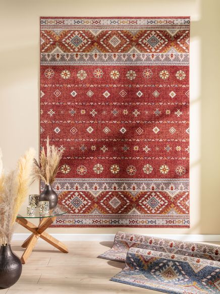 Roter Teppich mit geometrischem Muster an Wand, Glas-Holztisch mit Vasen und Deko im Raum.