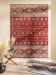 Roter Teppich mit geometrischem Muster an Wand, Glas-Holztisch mit Vasen und Deko im Raum.