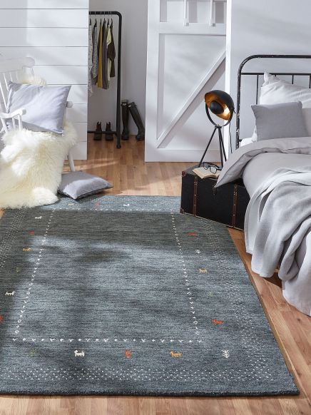 Blauer Teppich liegt auf Holzfußboden neben Bett, Stuhl mit Kissen, Lampe auf Koffer im Schlafzimmer.