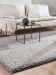 Beigefarbenes Sofa mit Kissen hinter schwarzem Tisch, Vase und Glas, auf grauem Teppich in hellem Raum